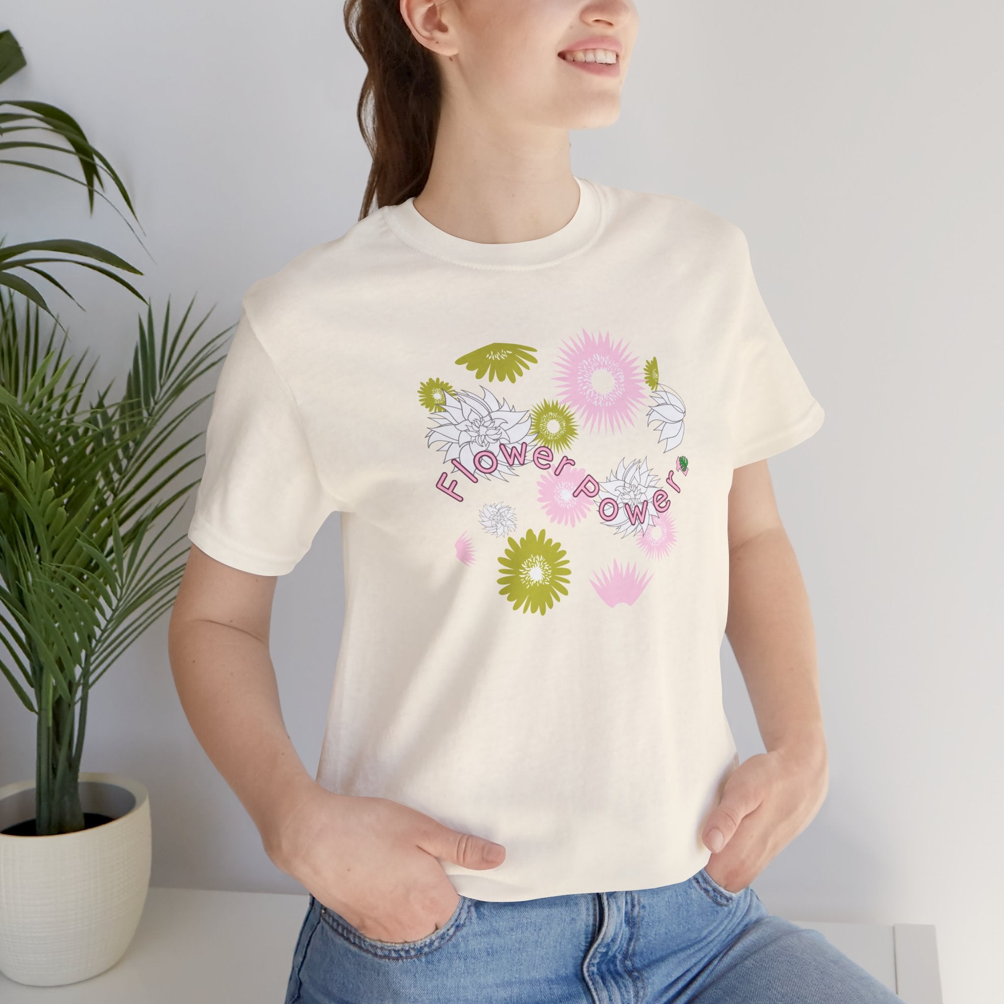 A person wearing a natural color tee shirt with the words flower power in pink.  There are also pink, white, and green flowers printed on the shirt.