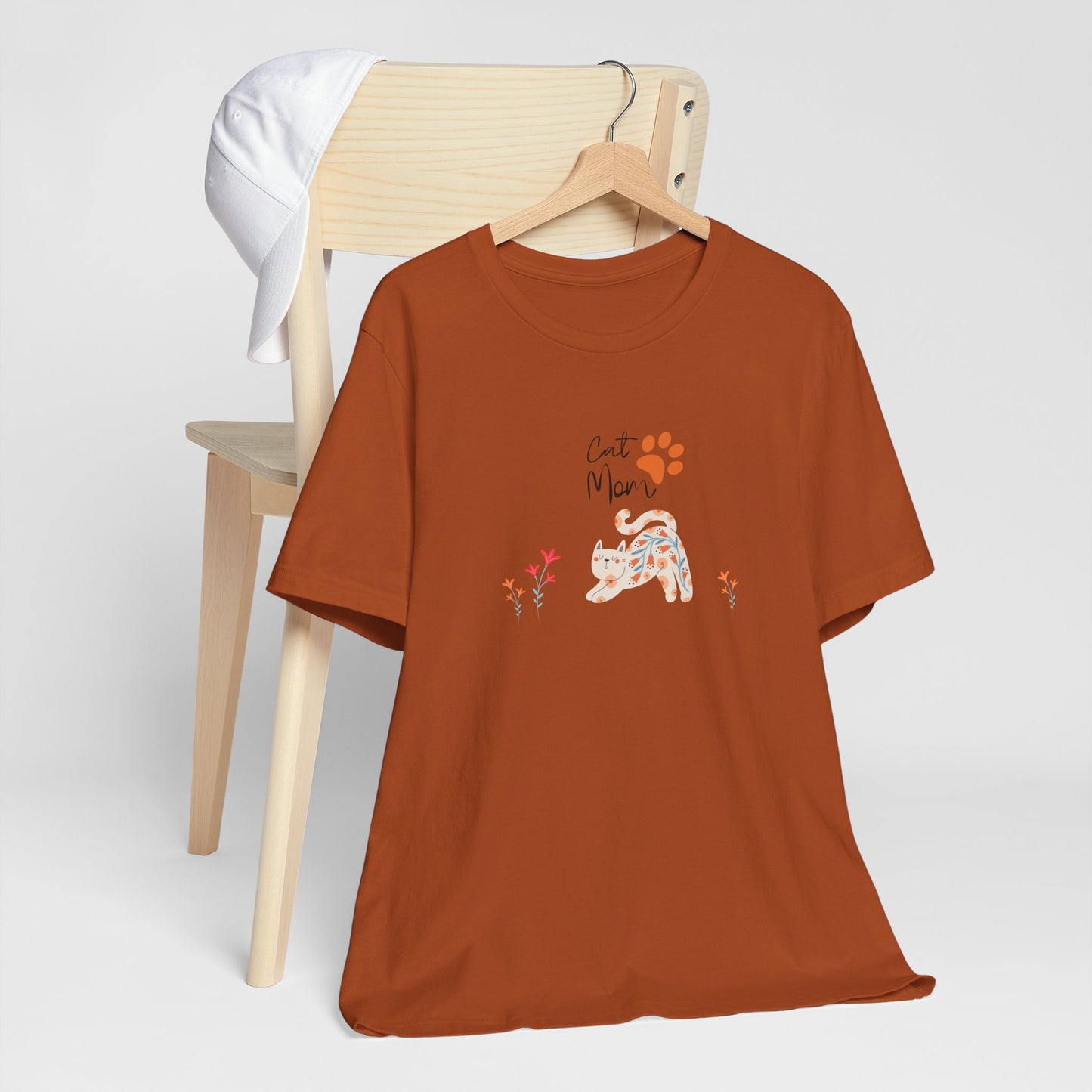 An autumn colored shirt with text that says "Cat Mom." There is also a cat print, a floral cat, and flowers around the cat design.