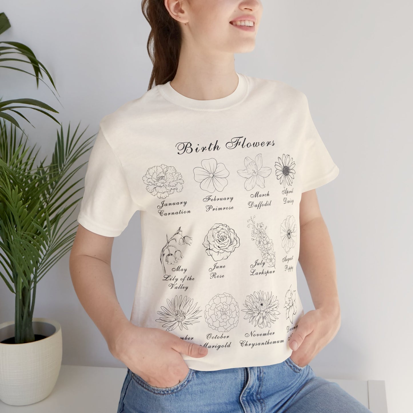 A person wearing a t-shirt in a natural colored tone and a printed design of birth flowers. Each month of the year is printed with a corresponding flower for that particular month. The t-shirt has a crew neck and short sleeves. It is also lightweight so it's perfect for layering. It also makes an excellent birthday, Mother's Day, Valentine's Day or Christmas gift.