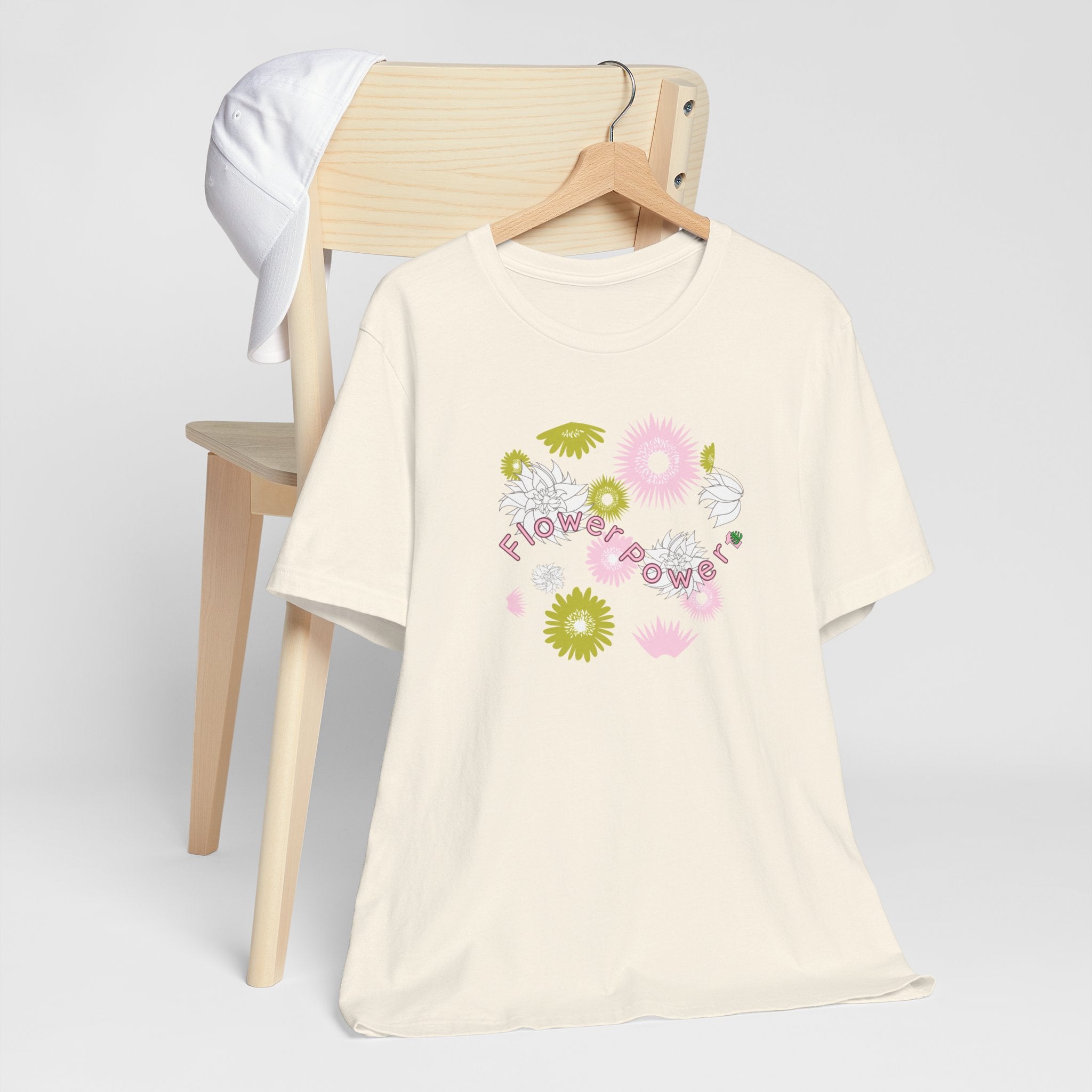 A hanging natural color tee shirt with the words flower power in pink.  There are also pink, white, and green flowers printed on the shirt.