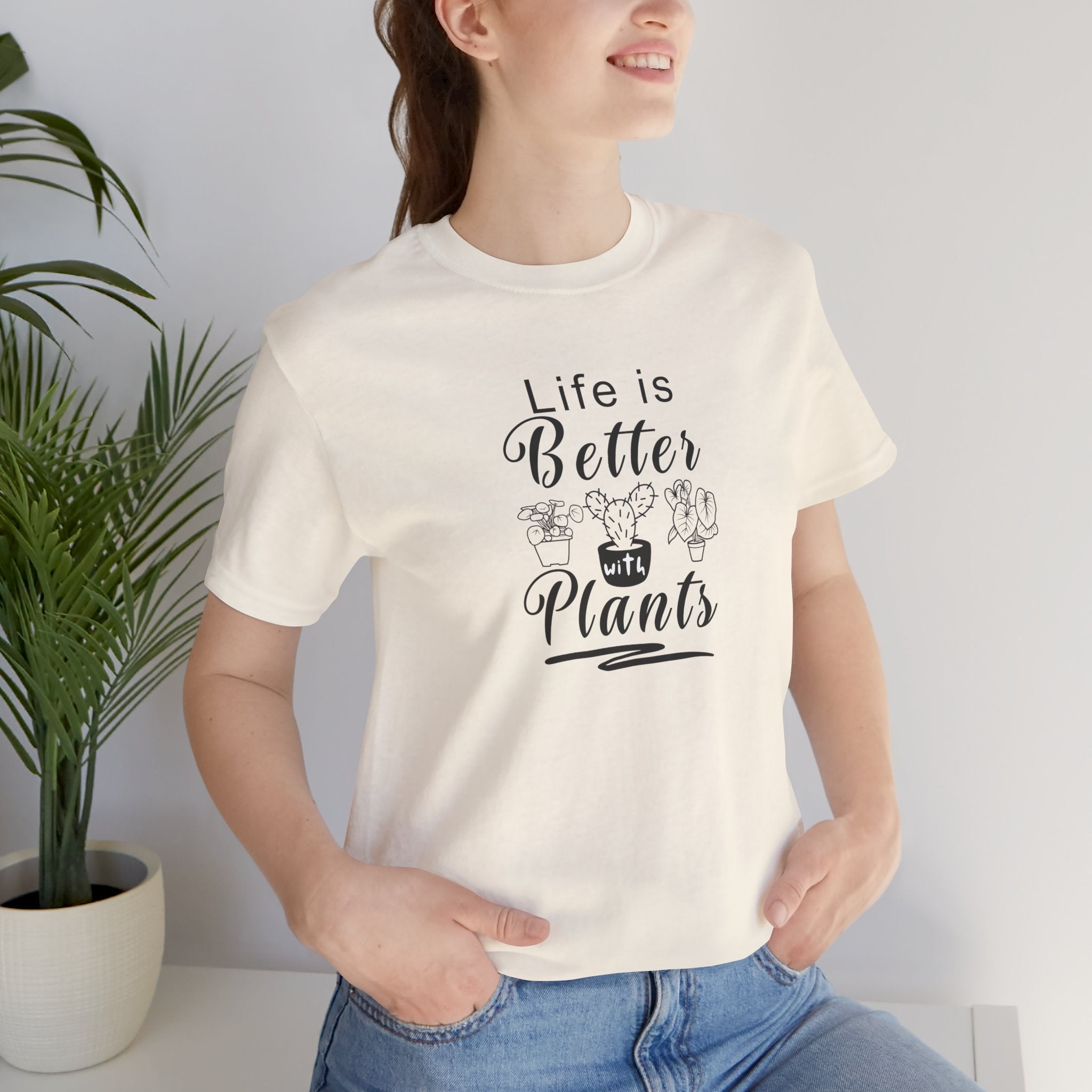 A person wearing a t-shirt with black text that says "Life is Better with Plants." The shirt comes in a natural color.