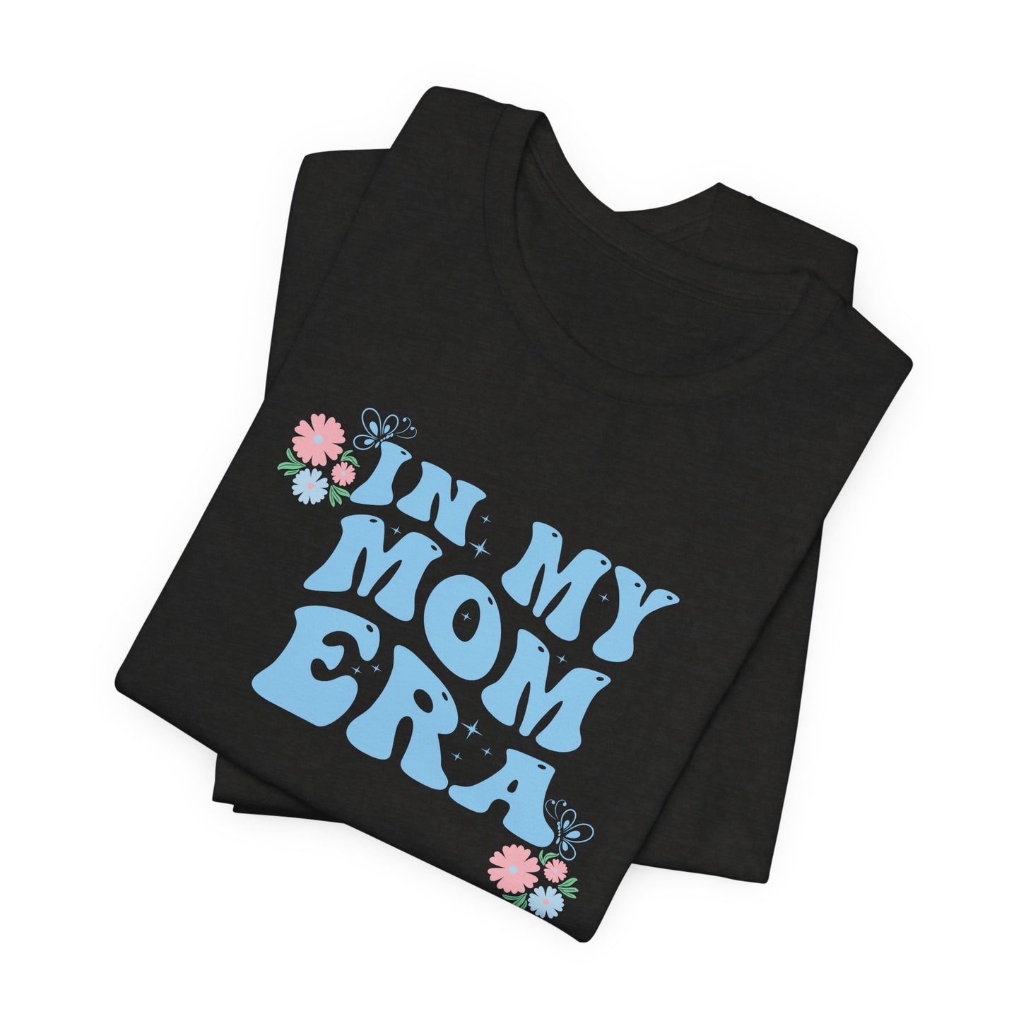 A folded graphic tee shirt with the words "In my mom era" printed in blue.