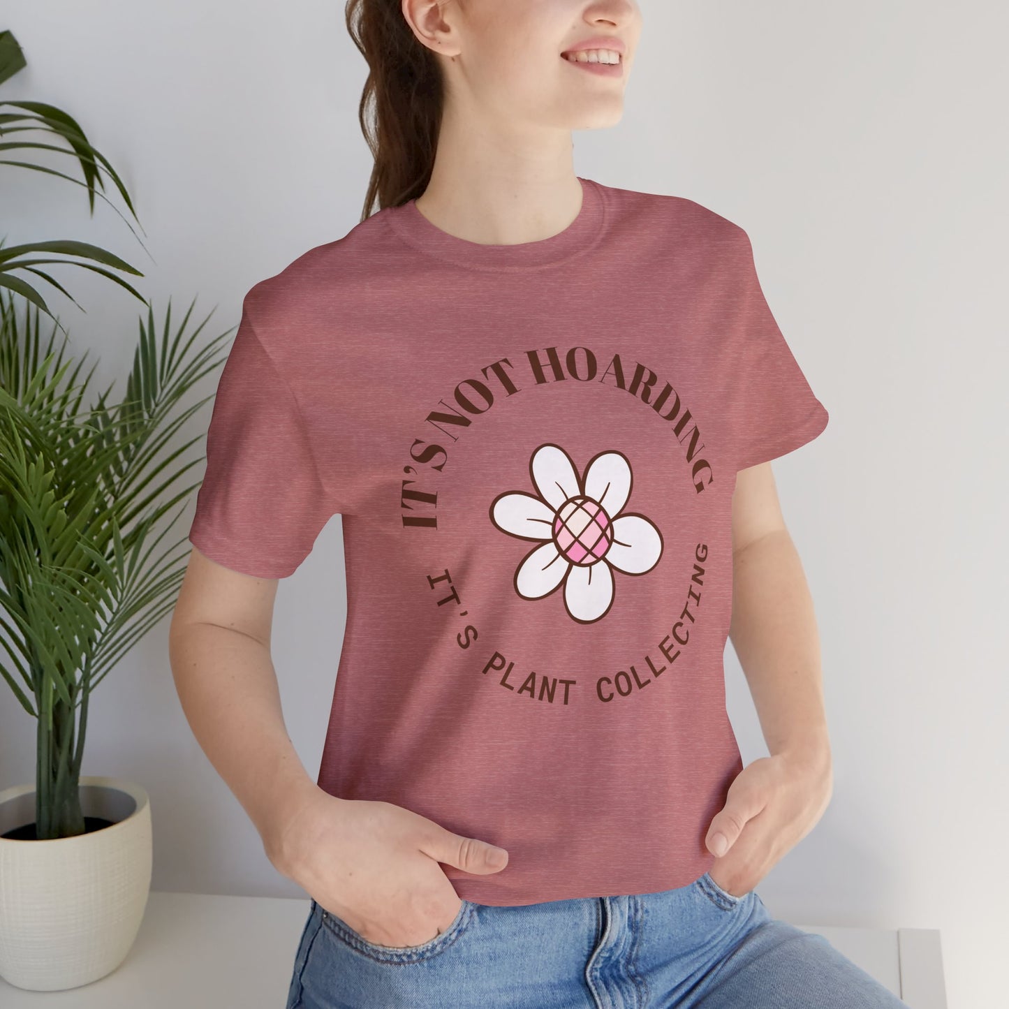 A heather mauve colored shirt with text that says "It's not hoarding" "It's plant collecting." The shirt design also has a groovy flower. The shirt is an excellent gift for teen and adult female houseplant collectors. Perfect for birthdays and Christmas gifts.