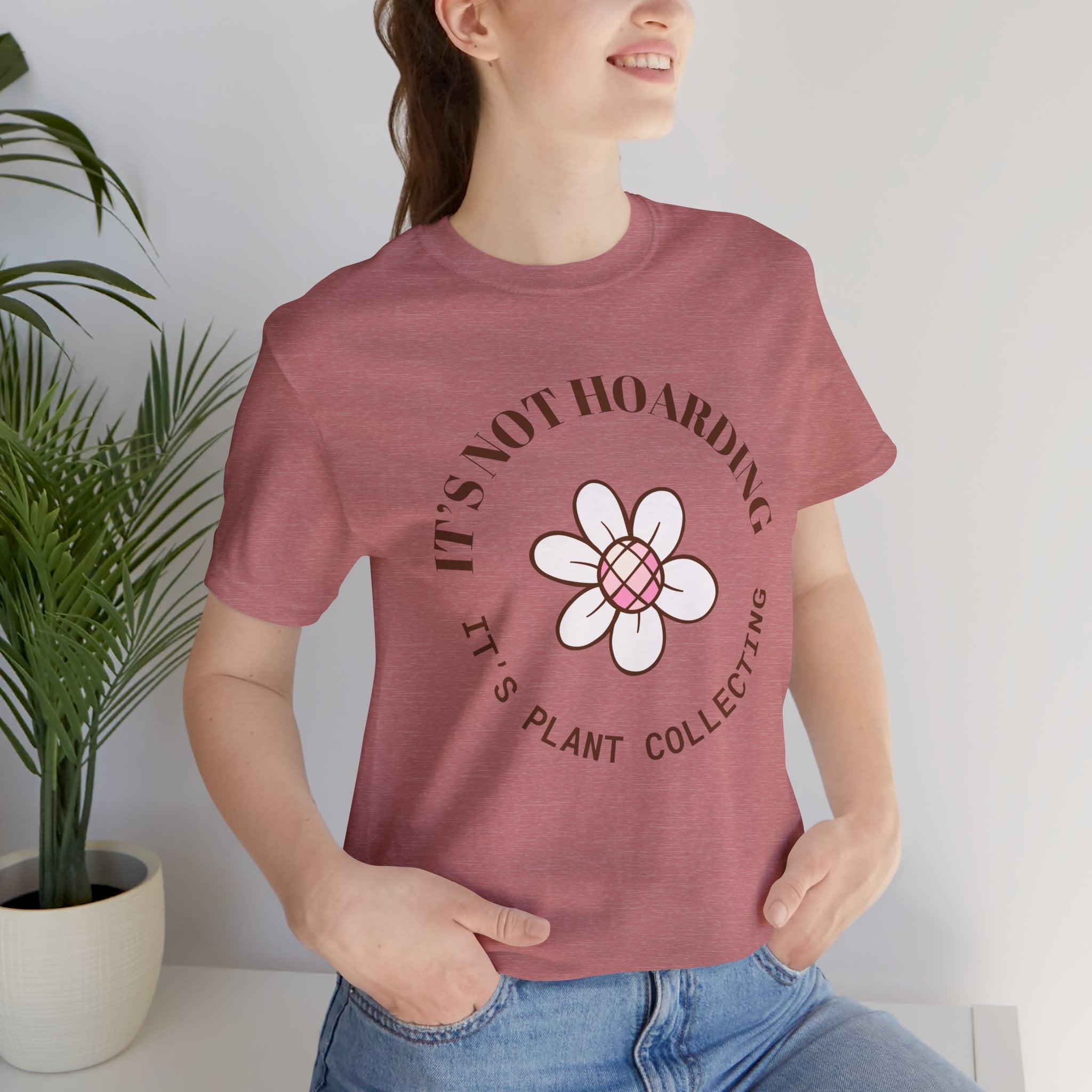 A heather mauve colored shirt with text that says "It's not hoarding" "It's plant collecting."  The shirt design also has a groovy flower. The shirt is an excellent gift for teen and adult female houseplant collectors. Perfect for birthdays and Christmas gifts.