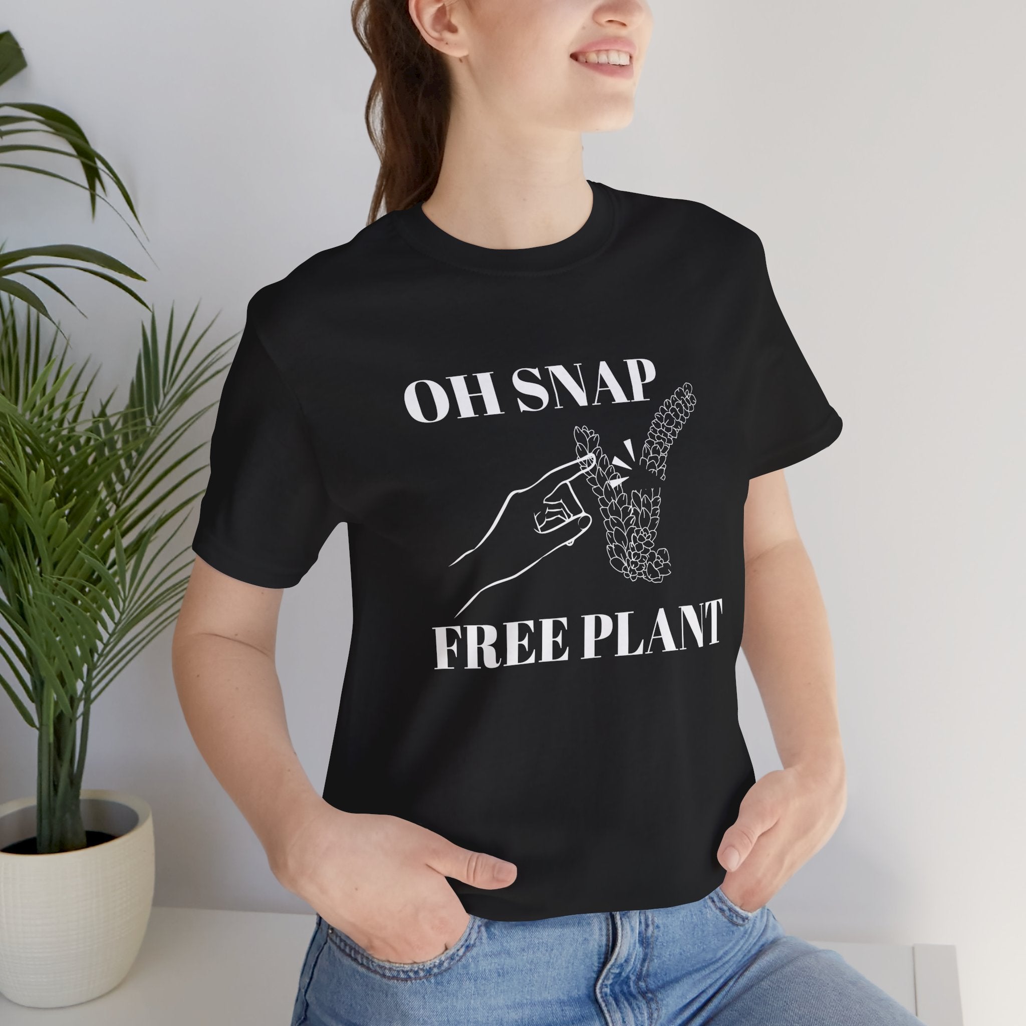 A student wearing a black colored shirt with text that says "Oh snap" "free plant."  The shirt design also has a burro's tail plant snapped in half and a finger pointing to it. The shirt is an excellent gift for birthdays and Christmas. House plant collectors love this funny t-shirt.
