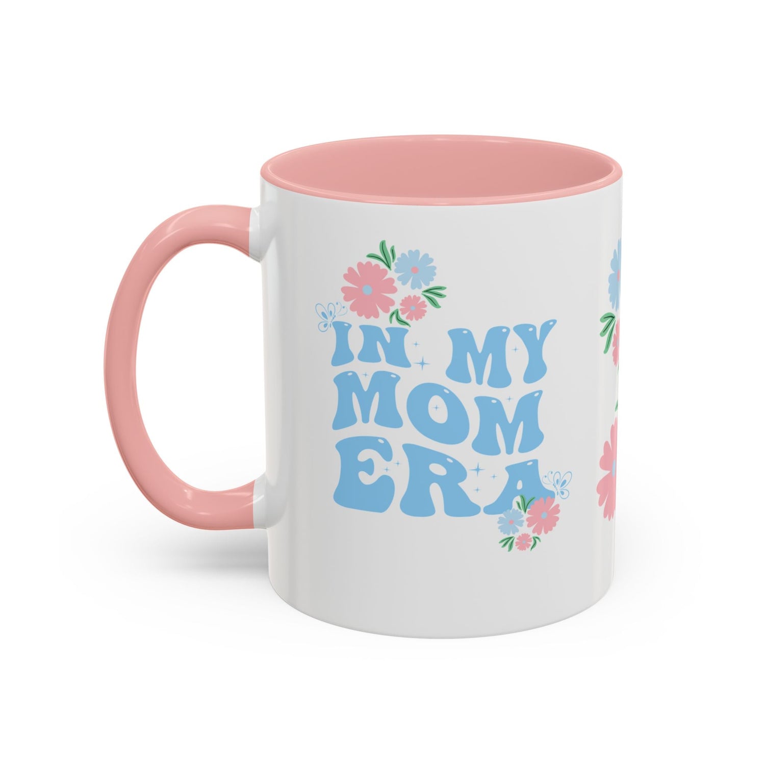 A ceramic mug with pink accent on the handle and inside the mug.  The front of the coffee mug has a floral design and the text "In my mom era"