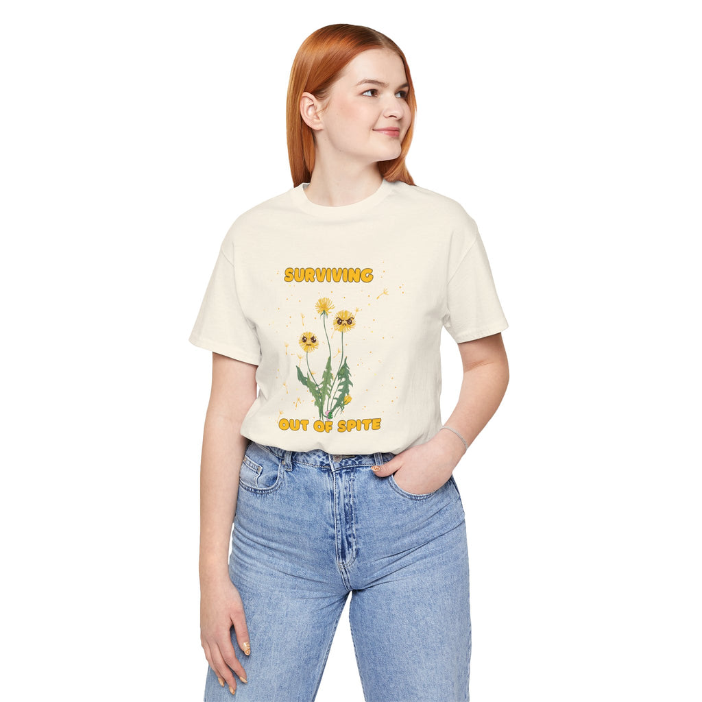 A person wearing a natural color t-shirt with yellow "surviving out of spite" funny text and dandelion plants with a funny look printed on the front of the shirt. 