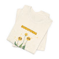 A folded natural color t-shirt with yellow "surviving out of spite" funny text and dandelion plants with a funny look printed on the front of the shirt. 