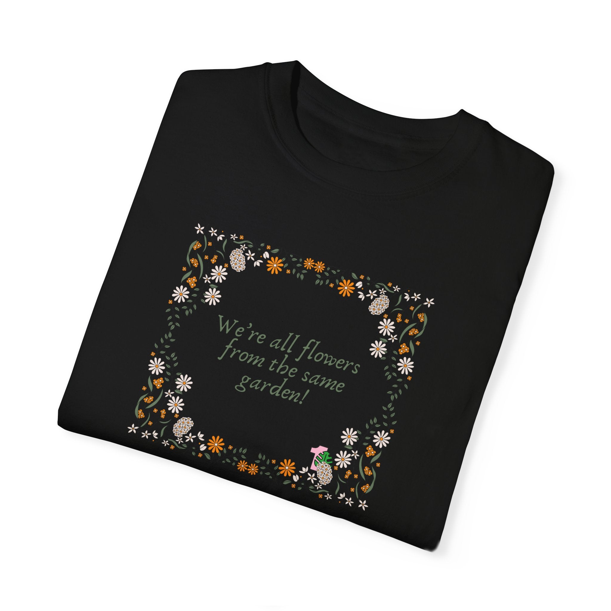 A folded black color tee shirt with a sentence that says "we're all flowers from the same garden!" This shirt makes an excellent gift for plant lovers