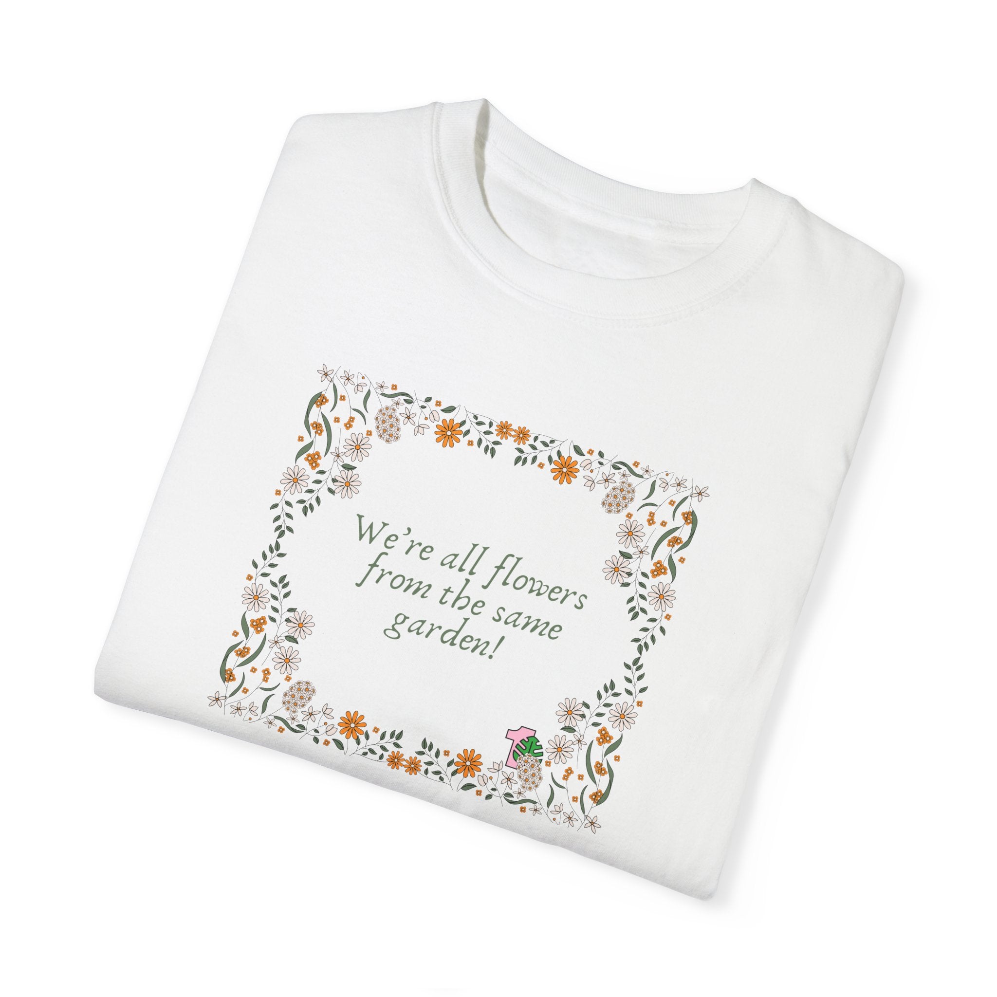 a folded white shirt with text that says "We're all flowers from the same garden!"  The text is surrounded by a floral frame. 