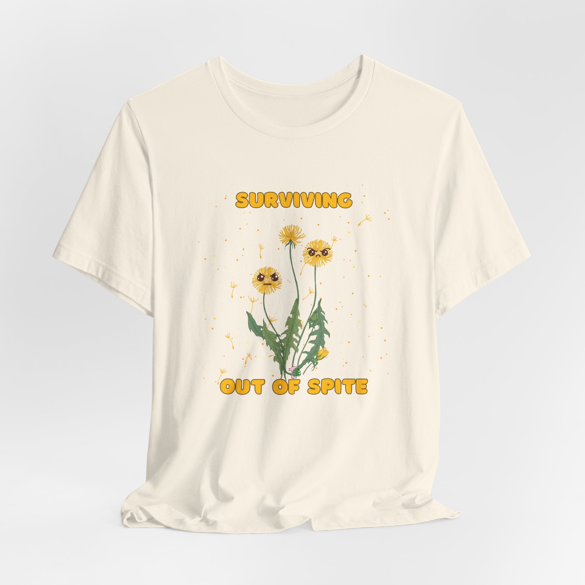 A natural color graphic t-shirt with yellow "surviving out of spite" funny text and dandelion plants with a funny look printed on the front of the shirt. 