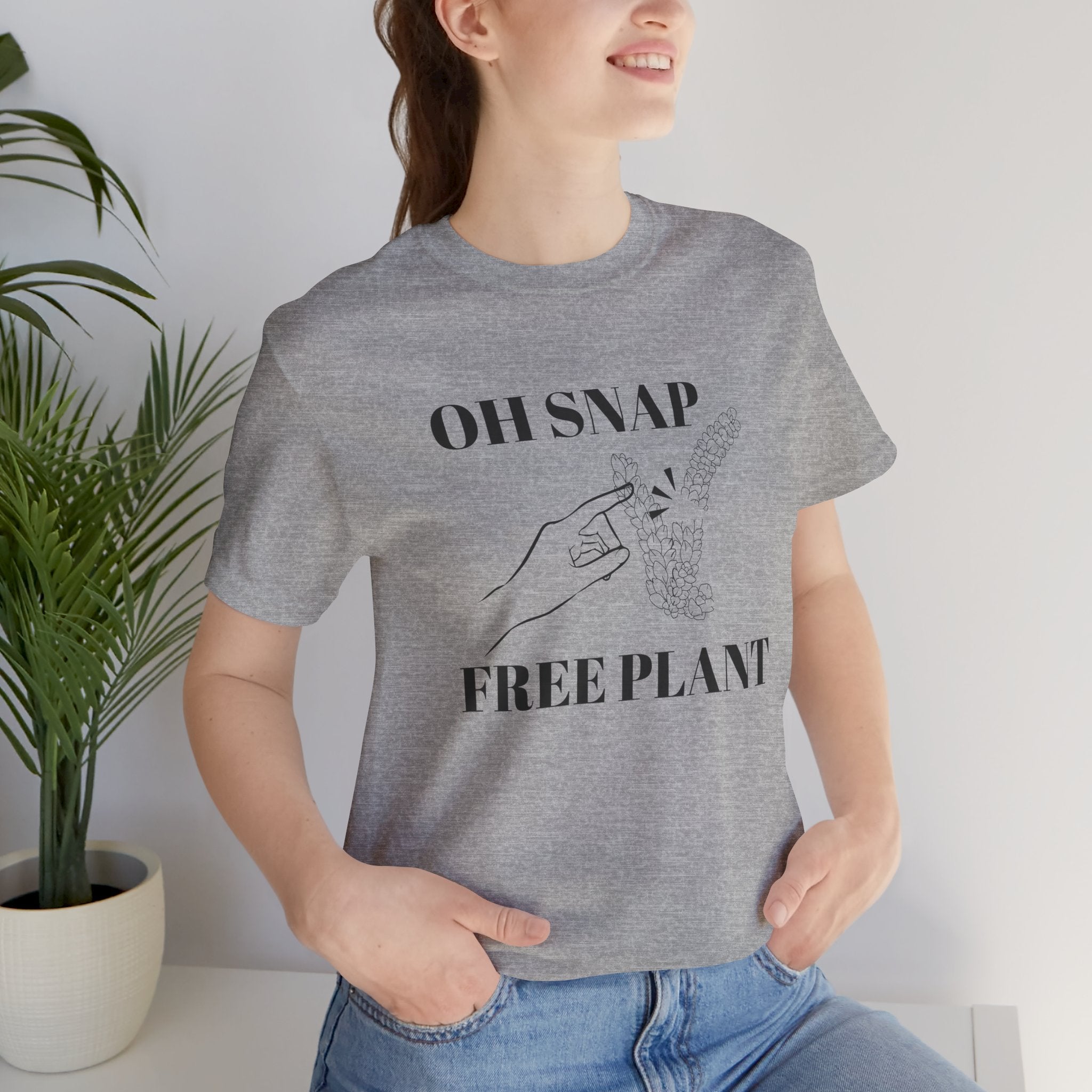 A woman wearing a funny t-shirt with an "OH SNAP FREE PLANT" design. There is also a lady's hand pointing to a burro's tail plant snapped in half. 