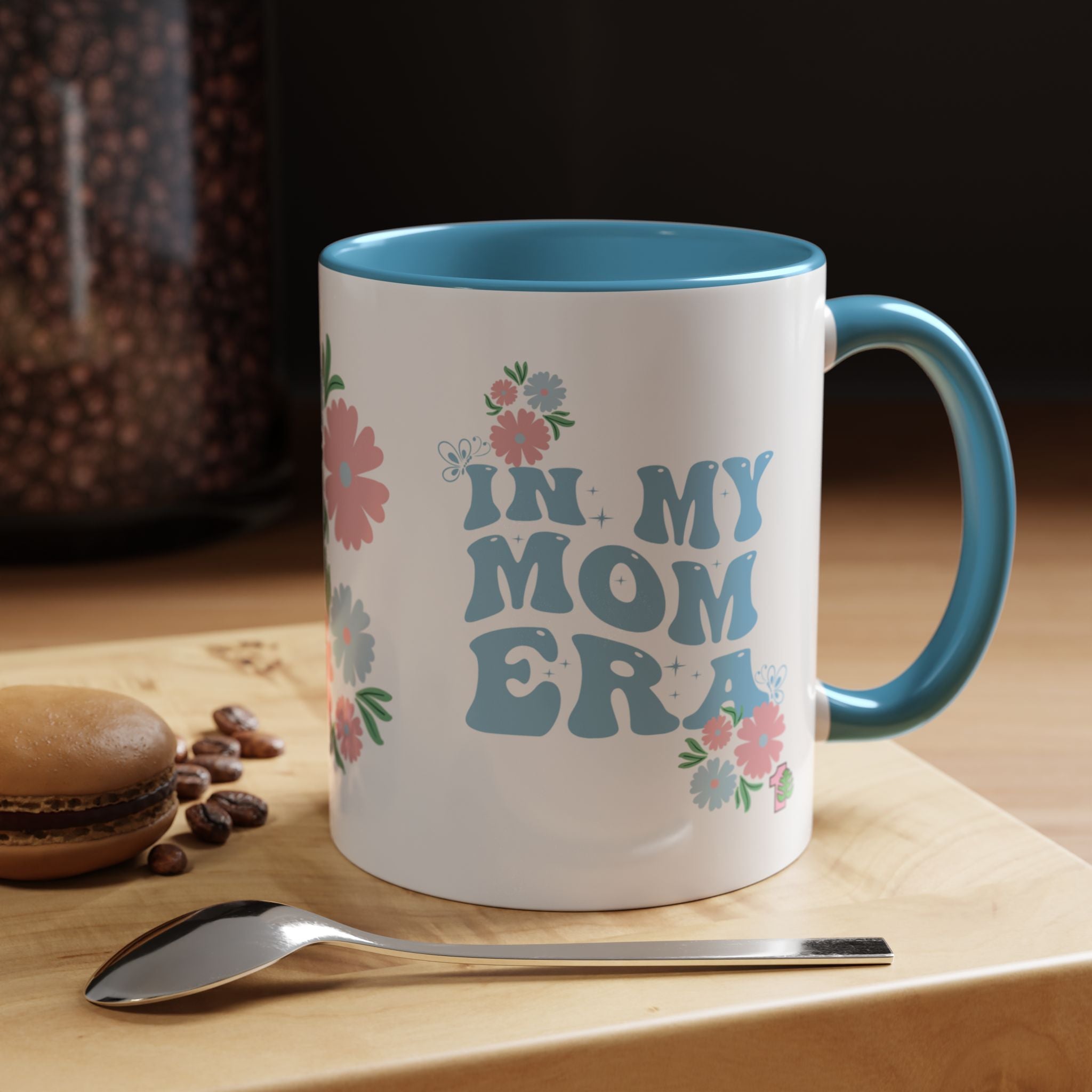 Mug with 'In My Mom Era' text on a wooden surface with coffee beans and a spoon.