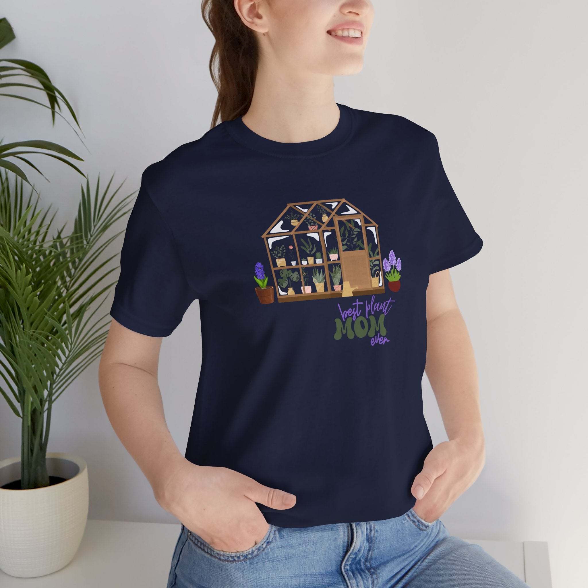 a person wearing a navy shirt with a greenhouse design and the words "best plant mom ever."  