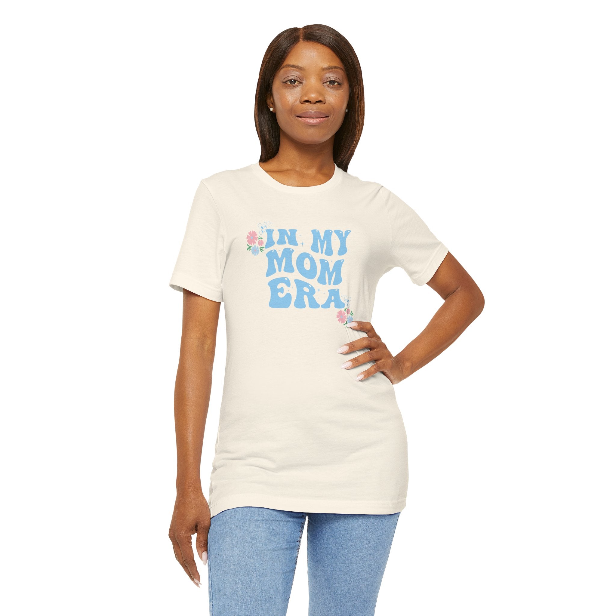 A person wearing a natural color graphic tee with the words "In my mom era" printed in blue. 
