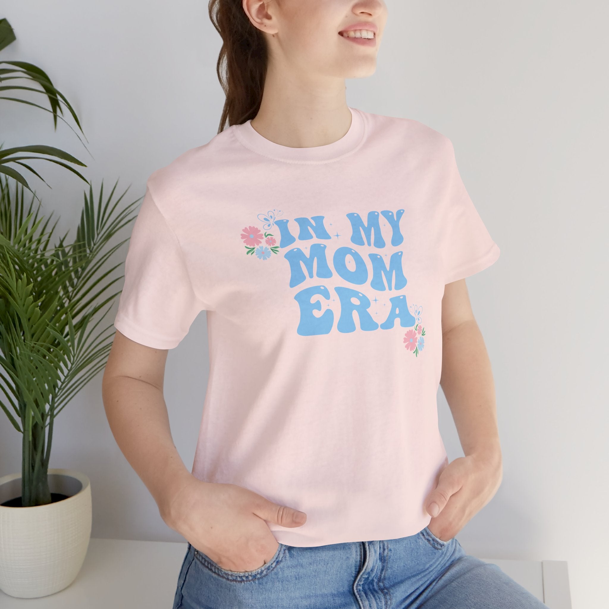A lady wearing a pink tee shirt with the words "In my mom era" printed in blue. This shirt makes an excellent t-shirt for soon to be moms.