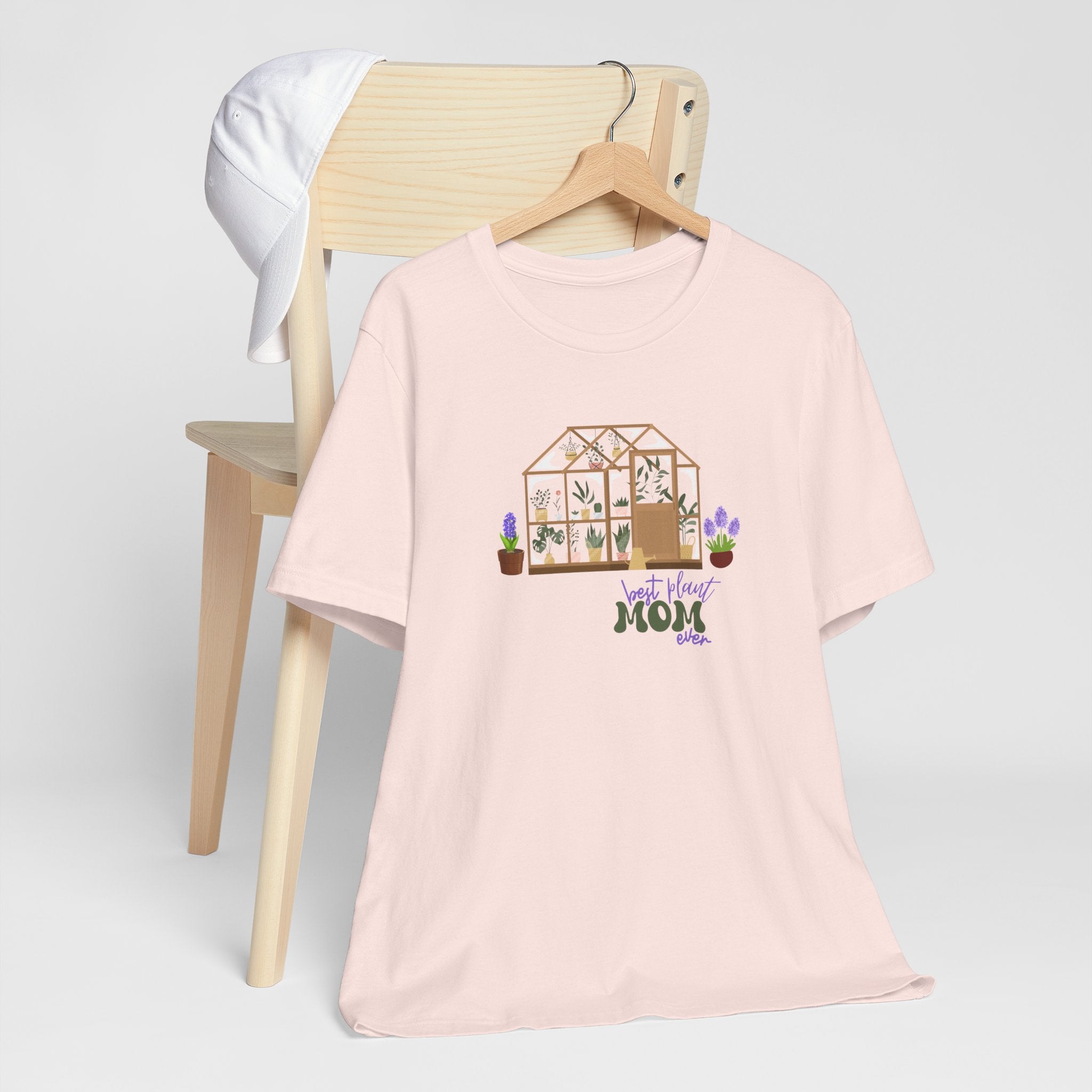 A jersey short sleeve tee in soft pink color with a printed greenhouse design.  There is also printed text that says best plant mom ever.