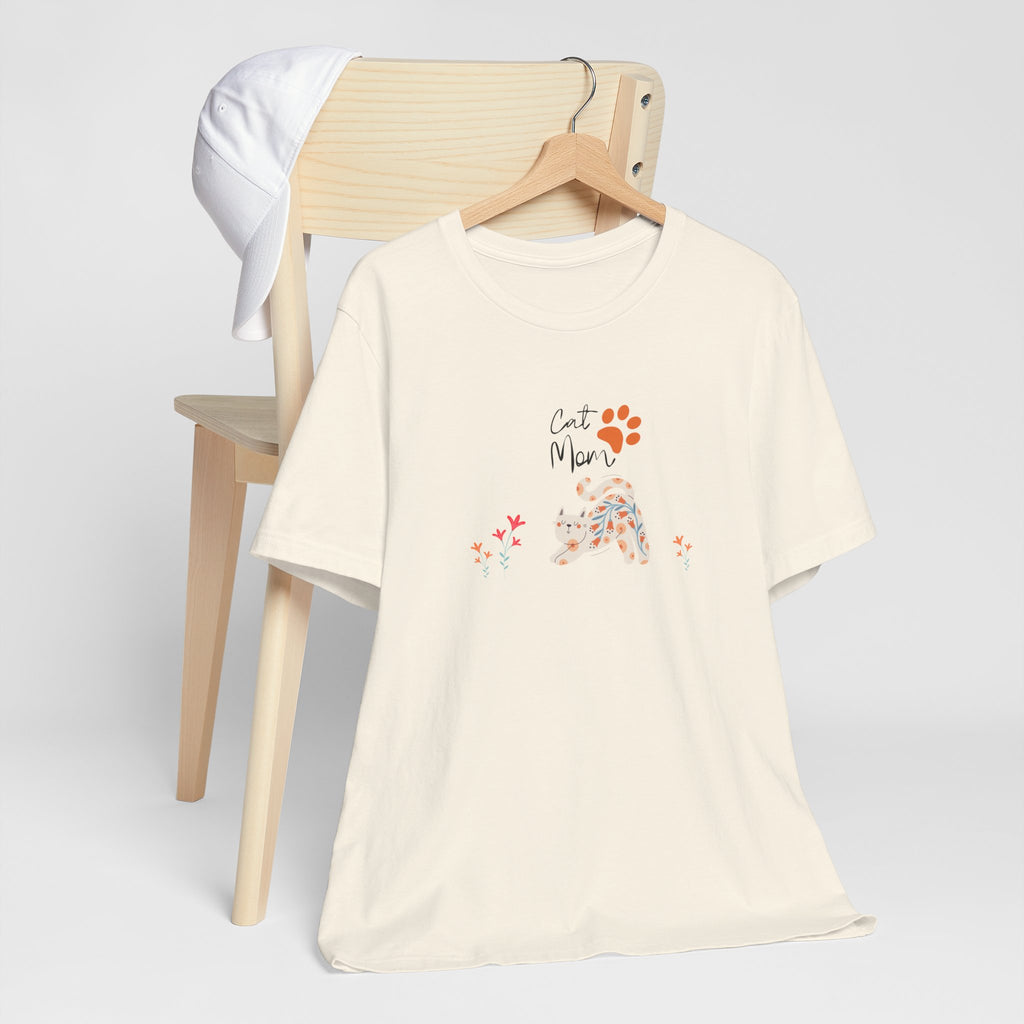 A natural color t-shirt with the words "cat mom," a floral cat, and some flowers printed on the front of the shirt.