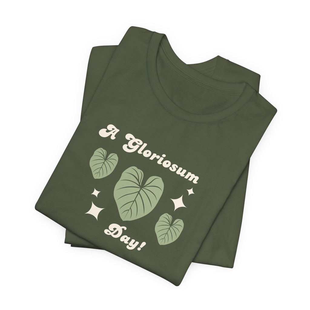 A folded military green t-shirt with text that says "A gloriosum day!"  The shirt design also has leaves from the philodendron gloriosum plant. 