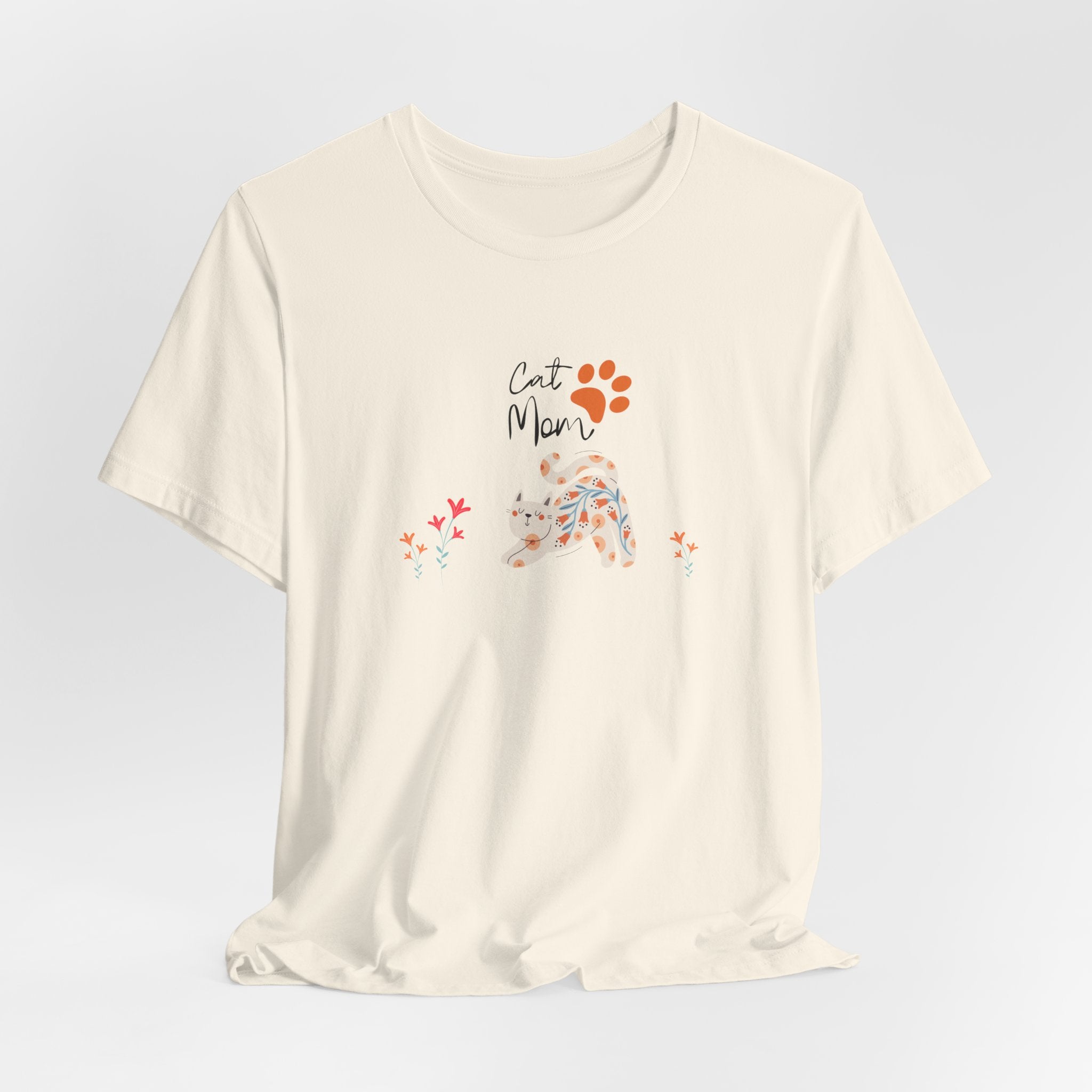 A natural color t-shirt with the words "cat mom," a floral cat, and some flowers printed on the front of the shirt.