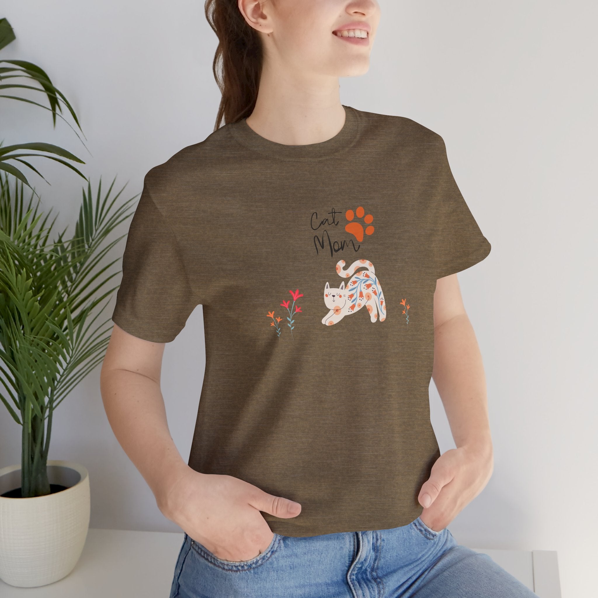 A person wearing a heather olive t-shirt with the words "cat mom," a floral cat, and some flowers printed on the front of the shirt.