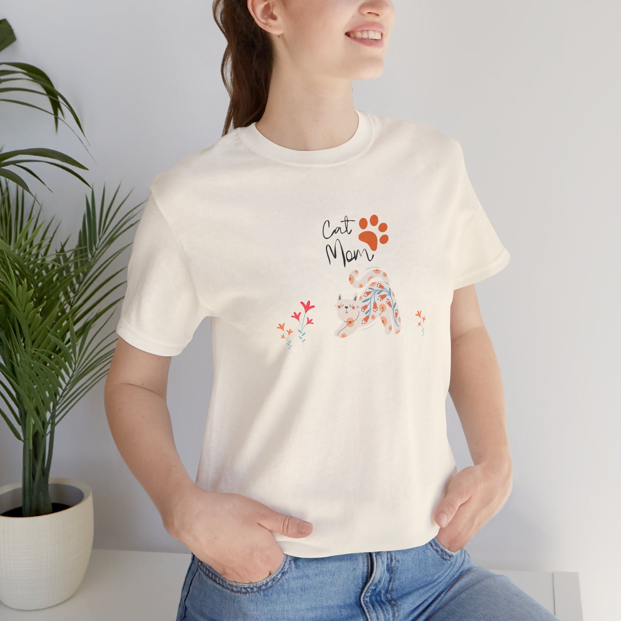 A person wearing a natural color t-shirt with the words "cat mom," a floral cat, and some flowers printed on the front of the shirt.