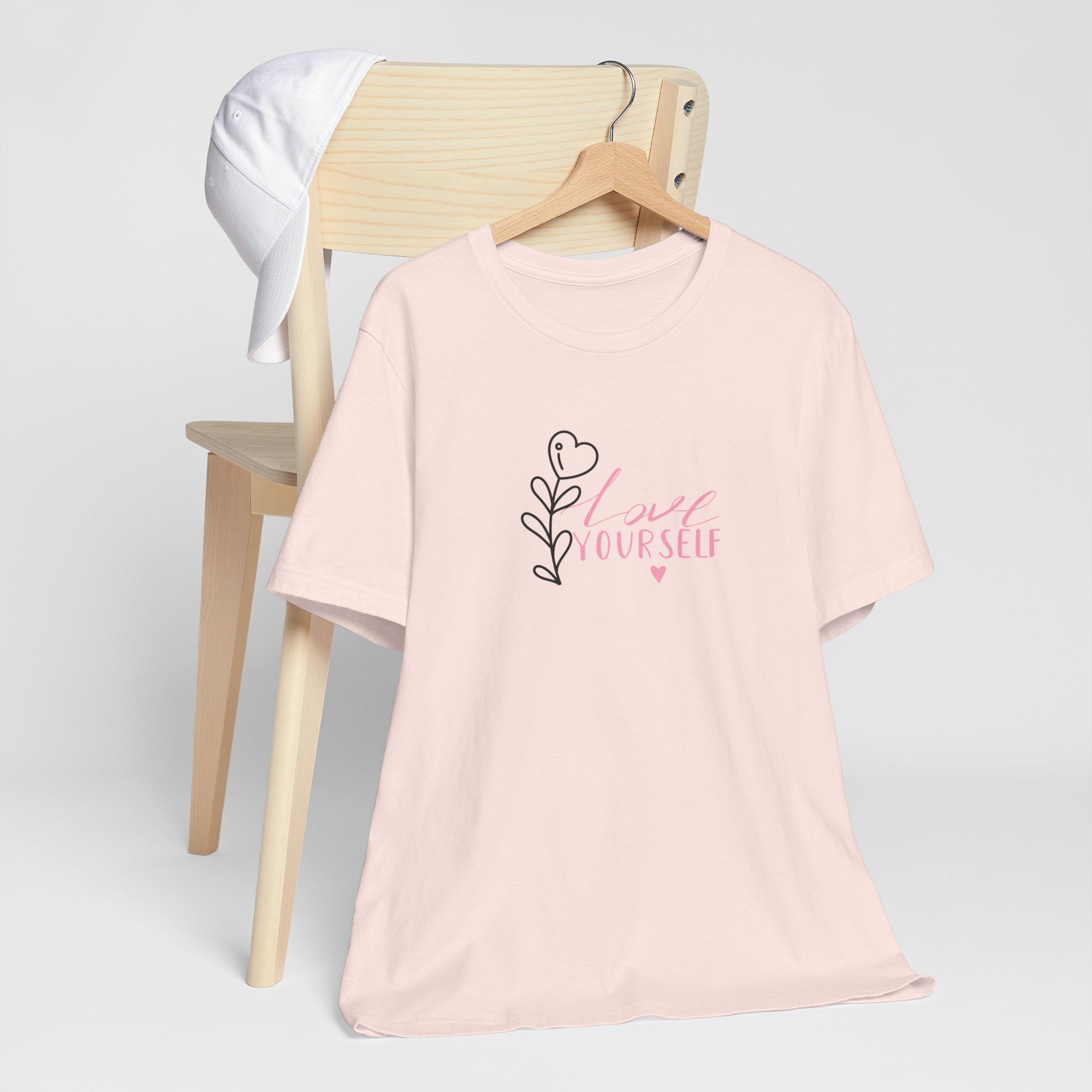 Picture of a soft pink tee shirt with the text love yourself.  This shirt encourages confidence in  the person that wears it and reads it. 
