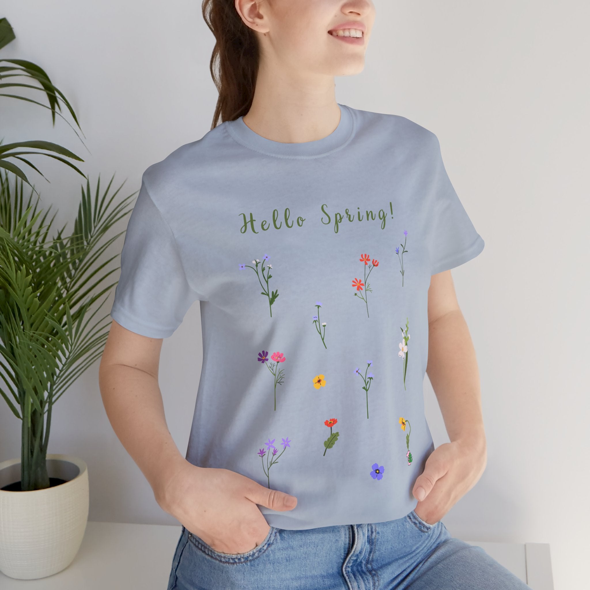 A close up of a woman wearing a crew neck t-shirt with wild flowers print and text that says "Hello Spring!" 
