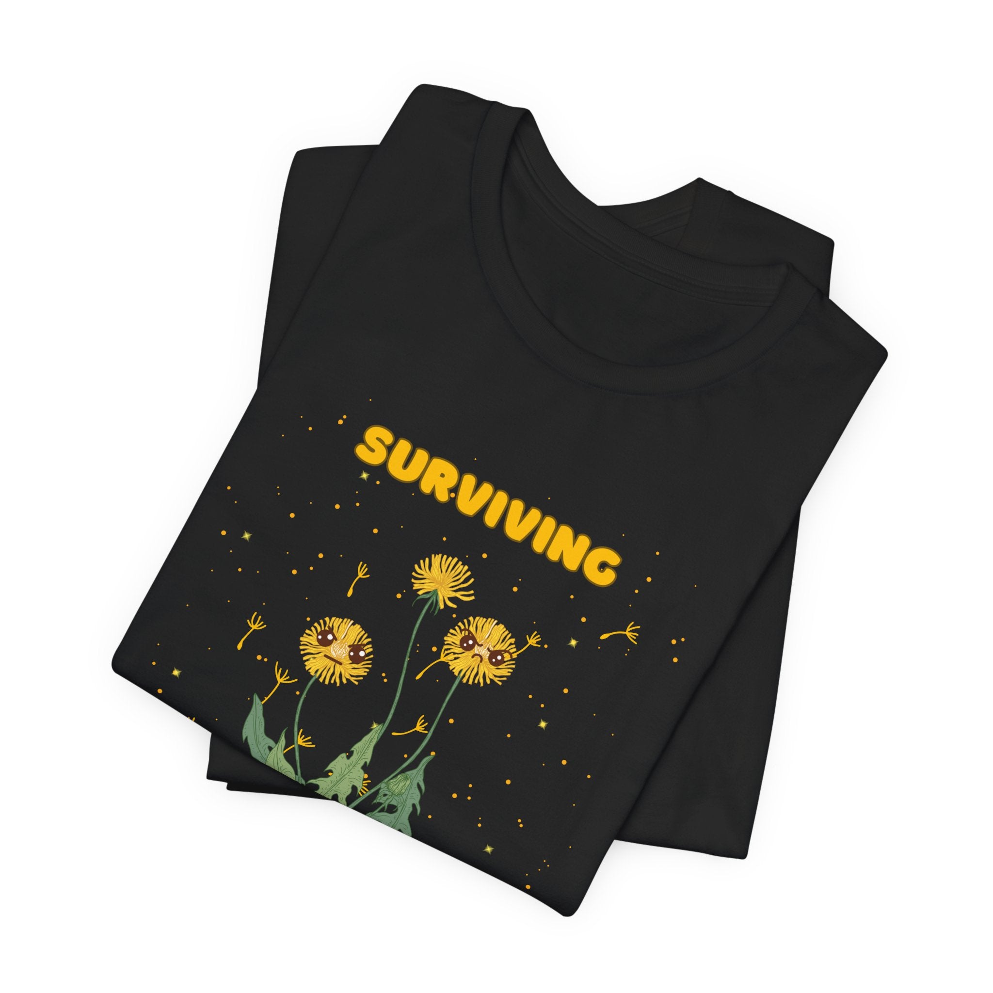 A folded black color t-shirt with yellow "surviving out of spite" funny text and dandelion plants with a funny look printed on the front of the shirt. 