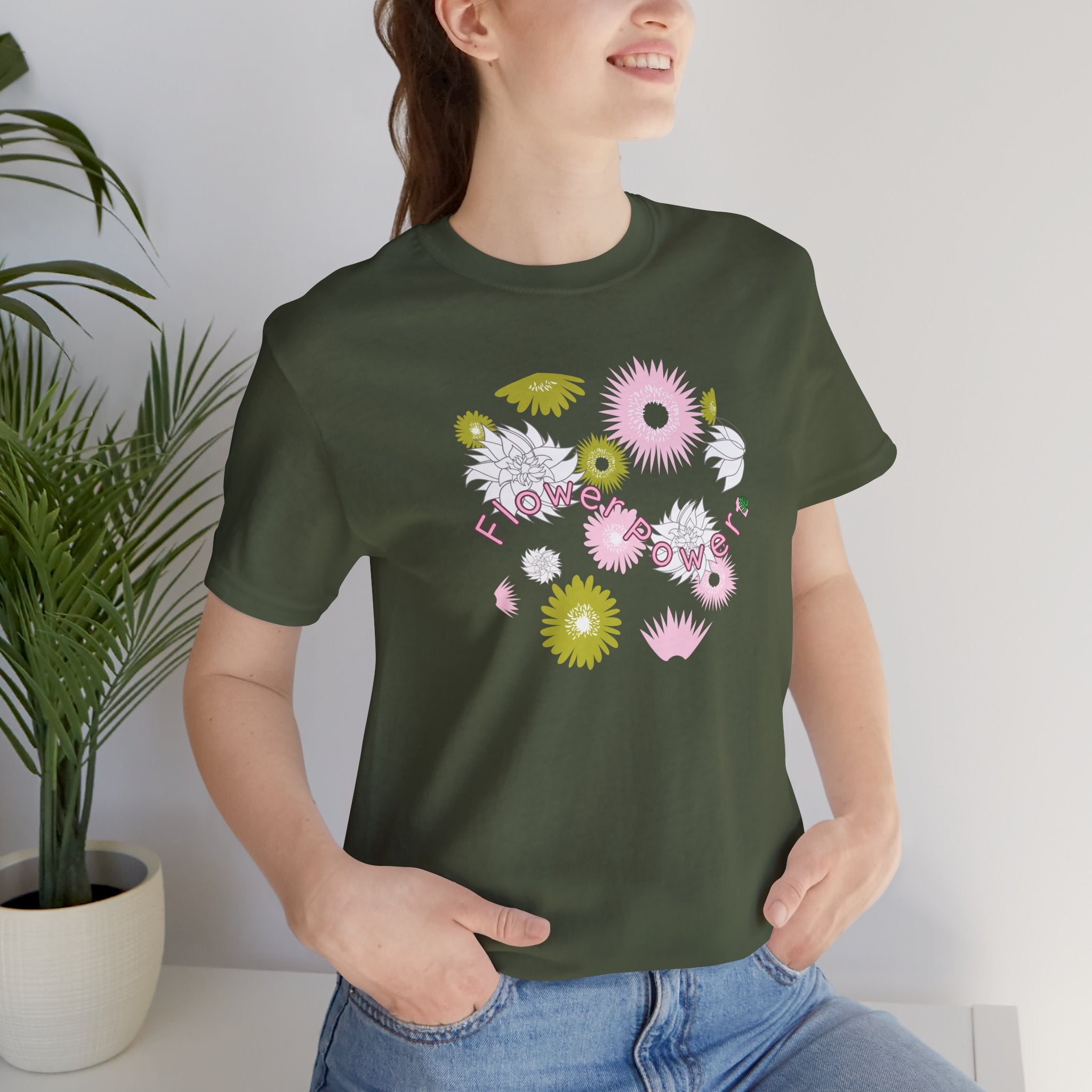 A person wearing a military green color tee shirt with the words flower power in pink.  There are also pink, white, and green flowers printed on the shirt. 