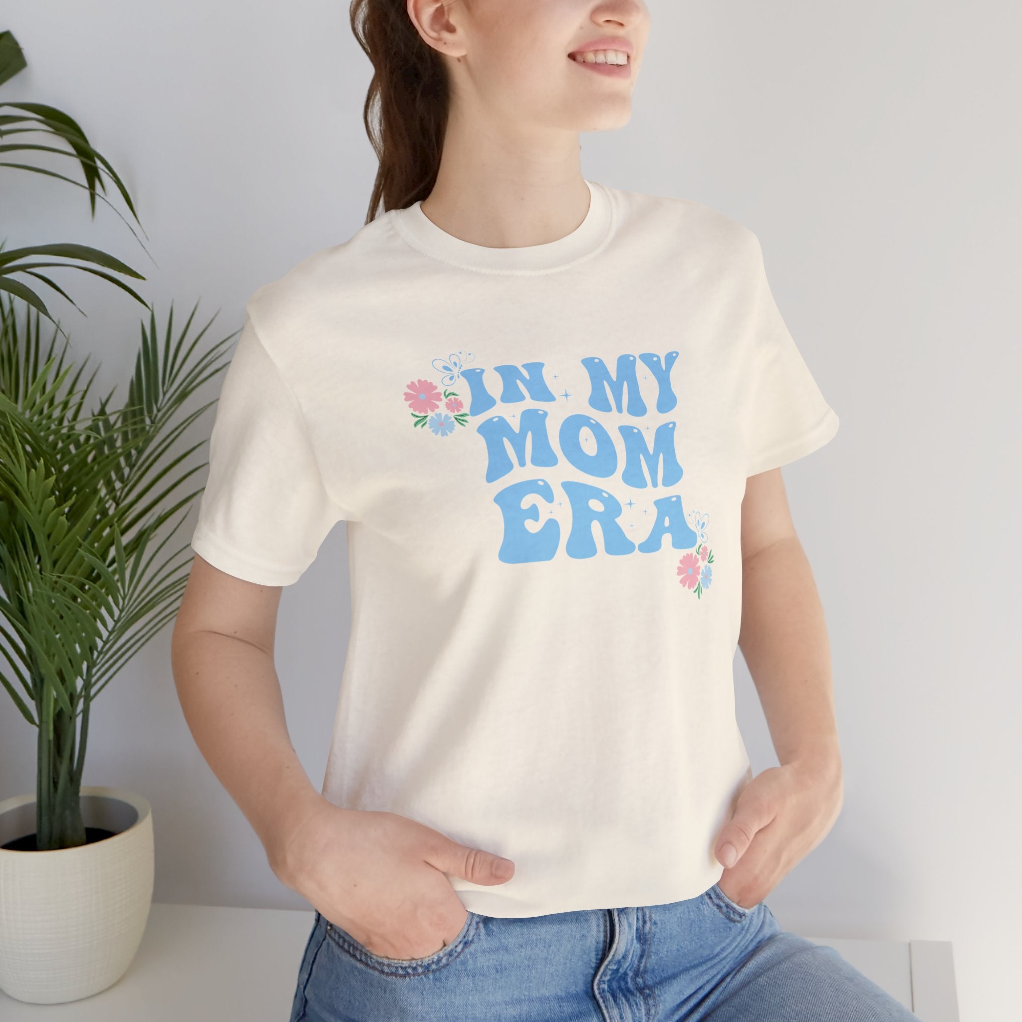a person wearing a natural color top with the words "In my mom era" printed in blue. 
