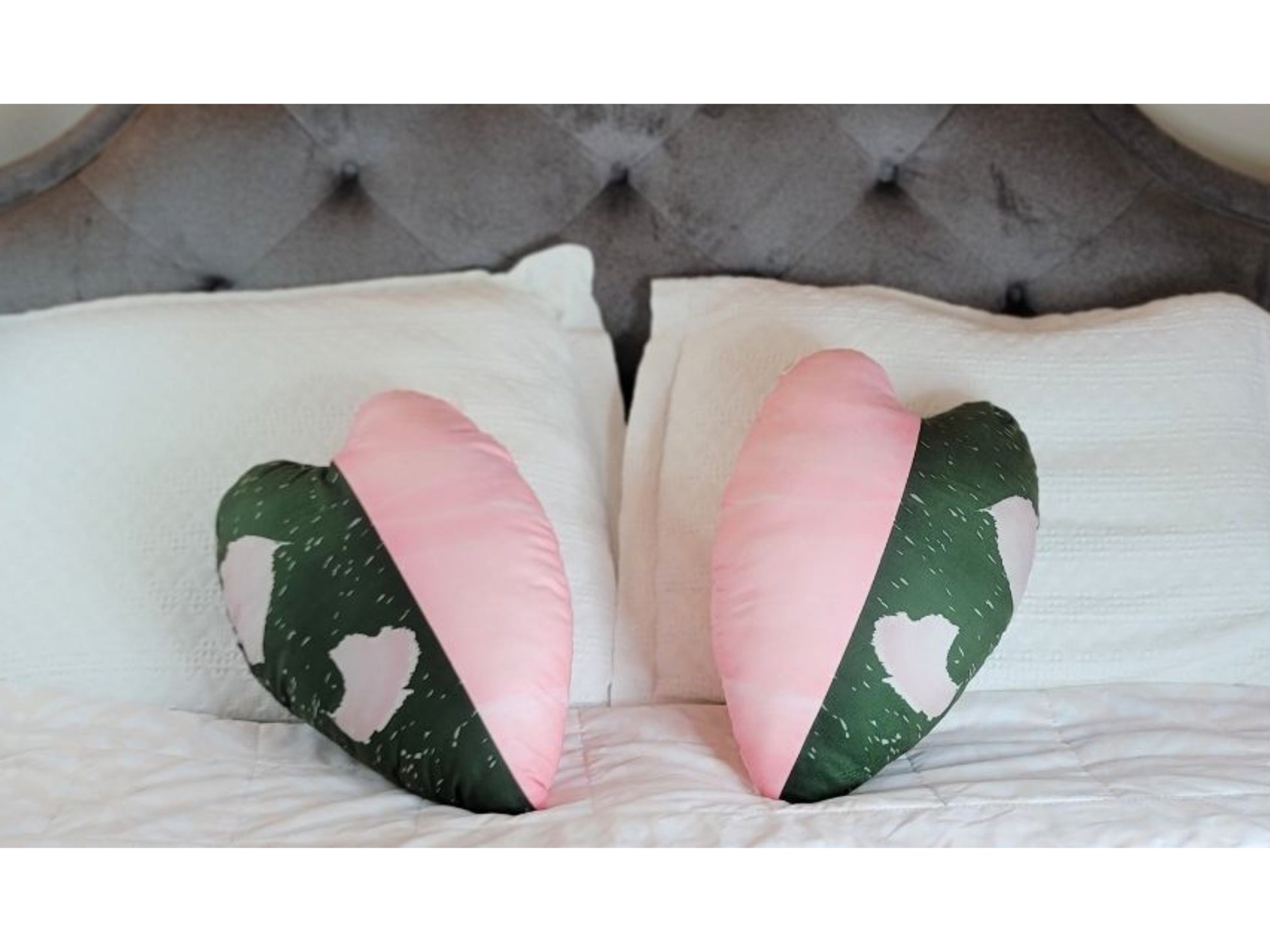 A pair of philodendron pink princess throw pillows. The pillows have a variegated design with one half of the pillow being pink and the other half being green.  Each pillow is a replica of a leaf print based on a natural philodendron pink princess plant leaf.  The pillows are placed on a bed with white bedding, adding a touch of color and whimsy to the bedroom decor. The pillows are soft, velvety, and plush.
