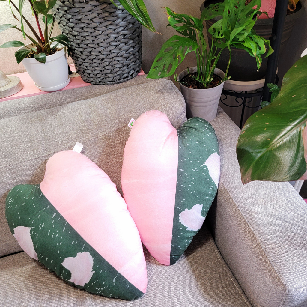 Two leaf-shaped cushions with pink and green design on a sofa, surrounded by potted plants.