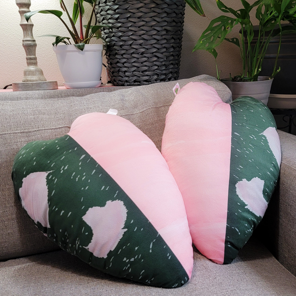 Heart-shaped pink and green cushions on a couch with plants in the background